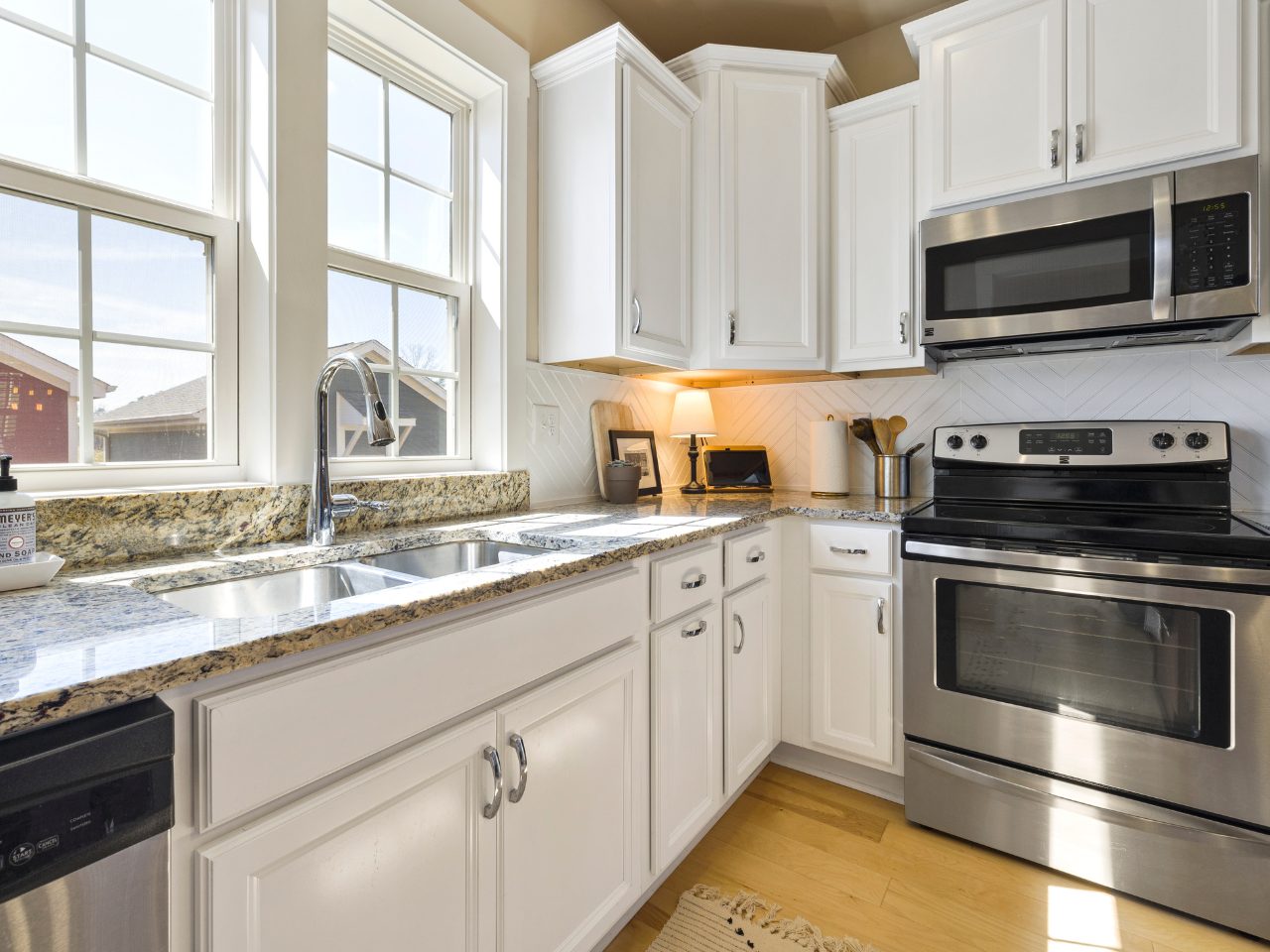 A bright white kitchen with granite countertops, stainless steel appliances, natural light, and clean uncluttered surfaces in modern home